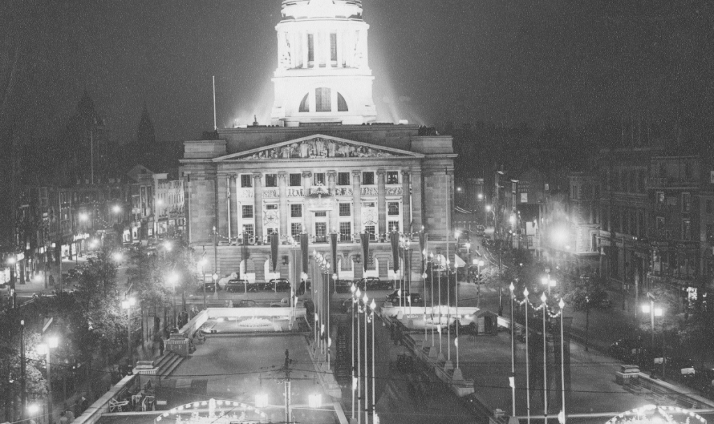 The image shows Old Market Square, dressed and illuminated in 1953 to celebrate the Queen’s Coronation (1953 credit: Nottingham Local Studies Library; Edgar Lloyd)