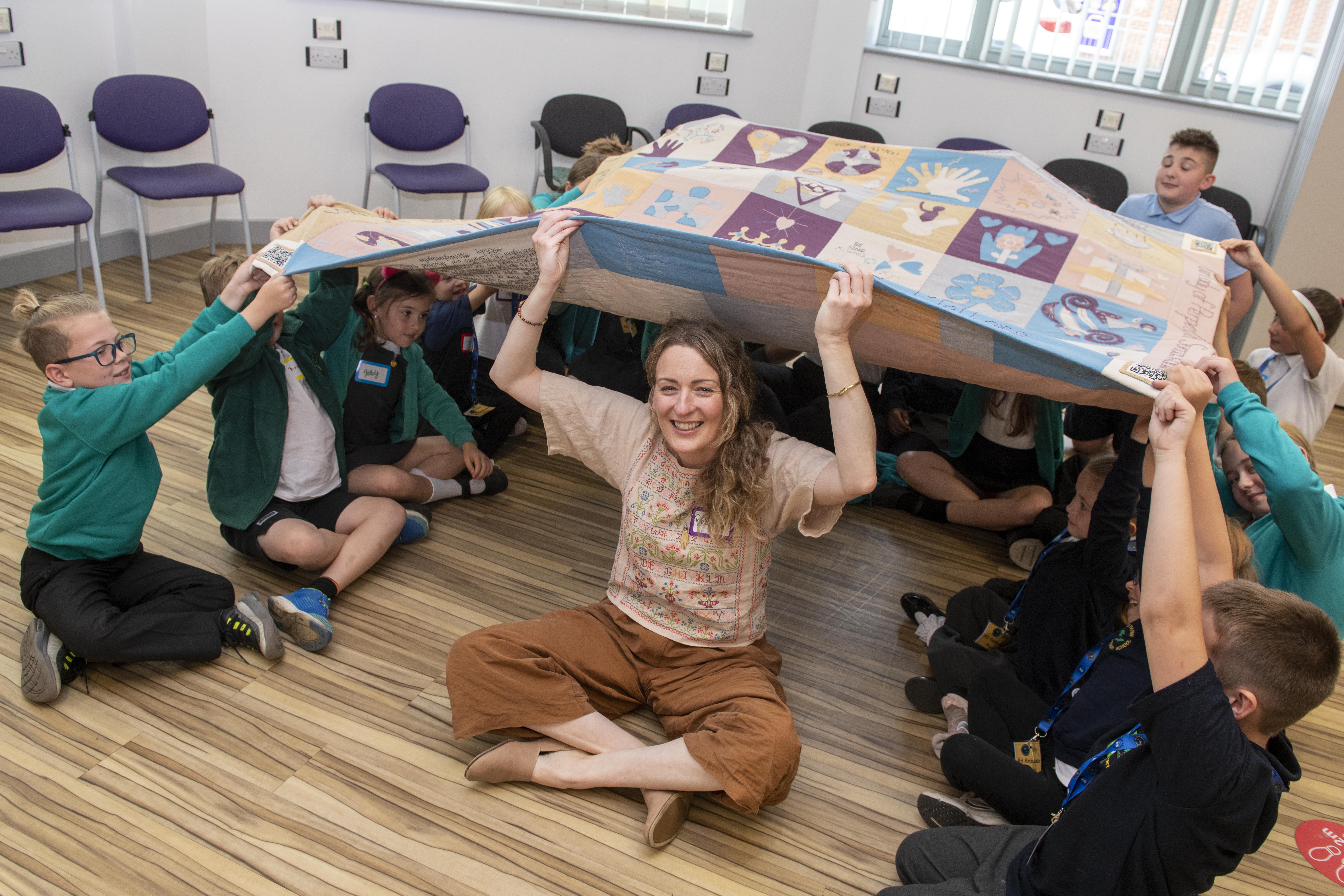 Artist and children with the 'Wrap yourself in Kindness Quilt