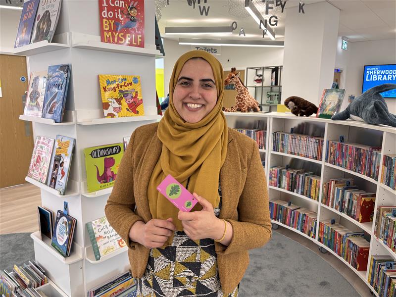 Neghat holding up a library card and smiling